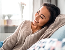 person smiling and sitting on the couch after dental crown restoration