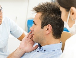 Man in dental chair holding jaw during emergency dentistry visit