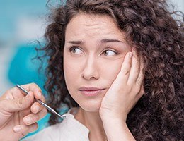 Woman in dental chair holding jaw before T M J therapy