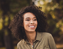 A young female wearing a green button-down blouse, smiles while standing outdoors