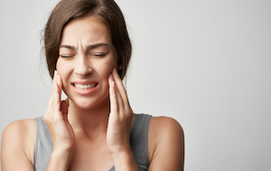 woman experiencing jaw pain, teeth clenched, white background