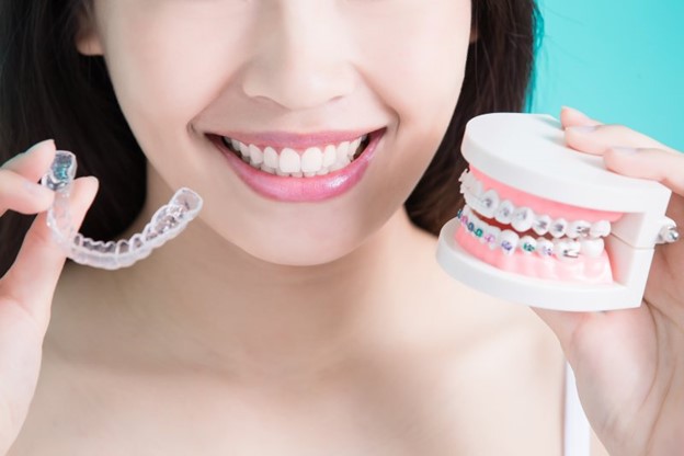 Woman holding Invisalign aligner and model of teeth with braces.