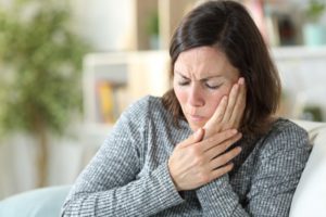 a woman holding her jaw due to the pain from TMJ disorder