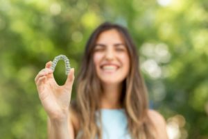 woman smiling and holding one Invisalign aligner
